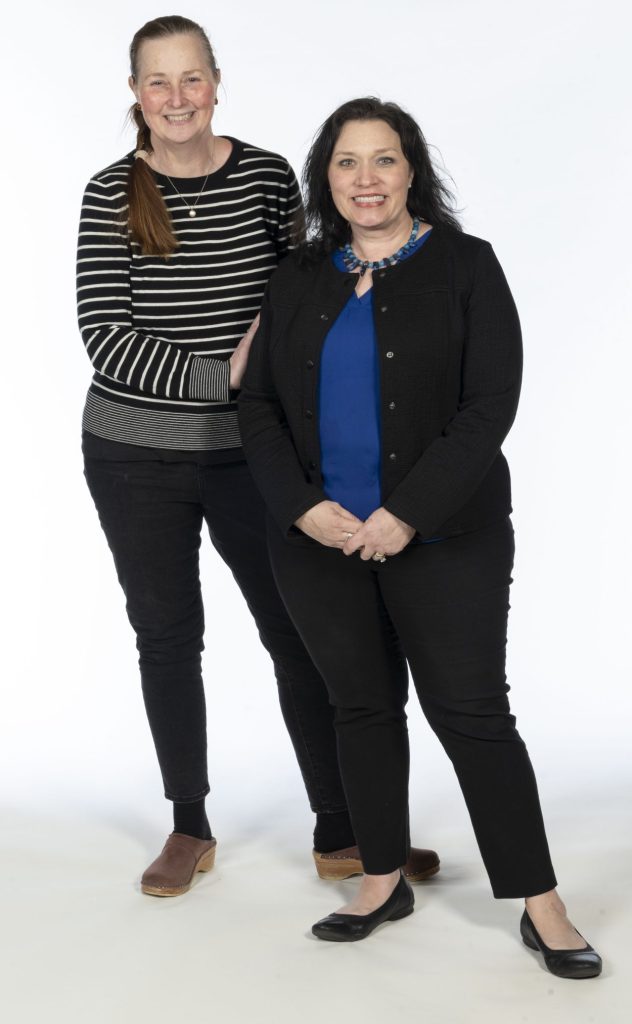 Two women stand smiling on a white background.