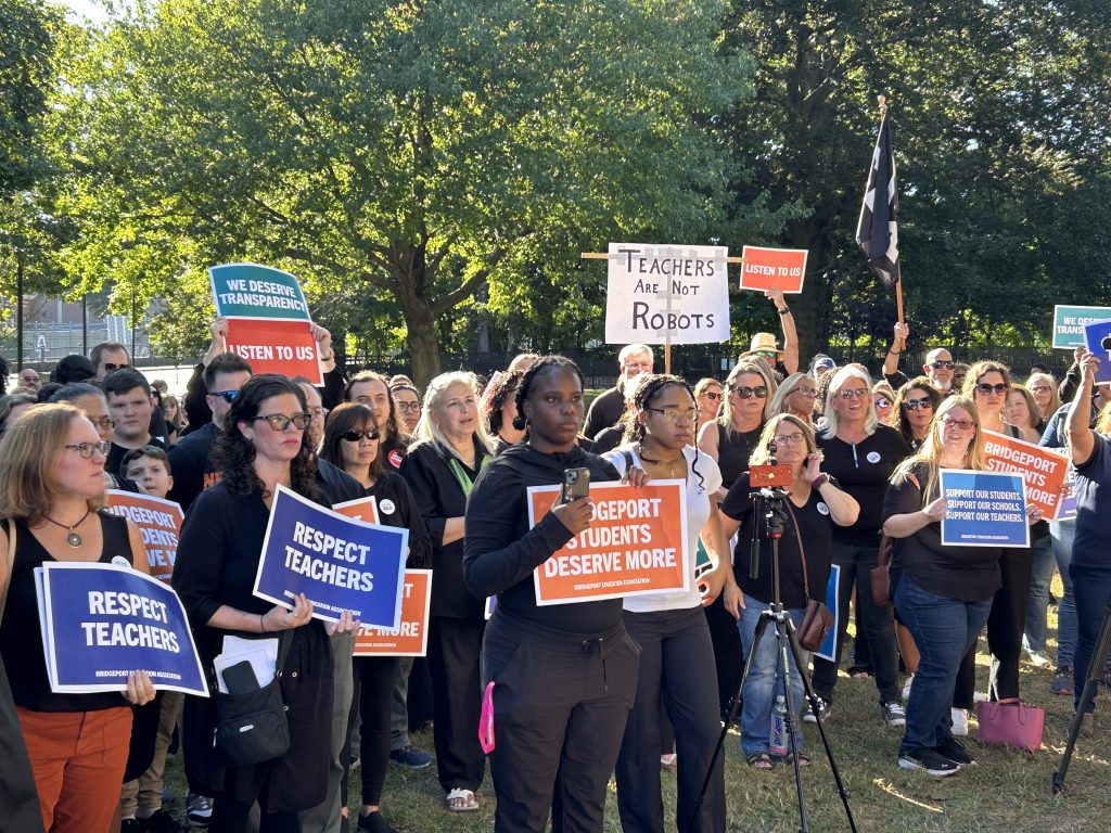 Wearing black and carrying signs that read, “Help us help our students,” “Bridgeport students deserve more,” and “Respect teachers,” teachers, parents and community members from across the city protested outside City Hall calling for actions to elevate education in Bridgeport.